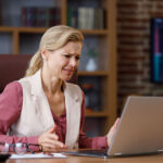 Lady stressed about paying care home fees at laptop